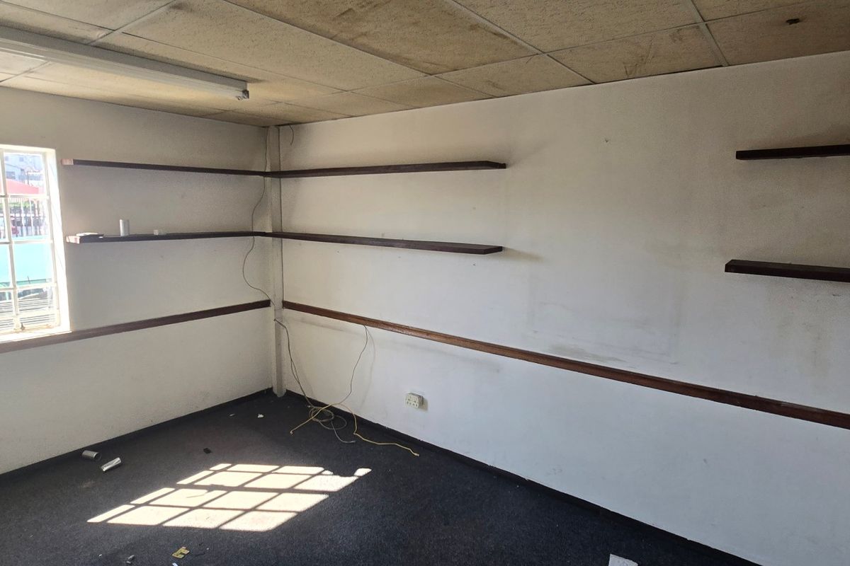 Empty office space featuring built-in shelving, dado rails, and security-barred windows, requiring cosmetic updates to the walls, ceiling, and flooring.