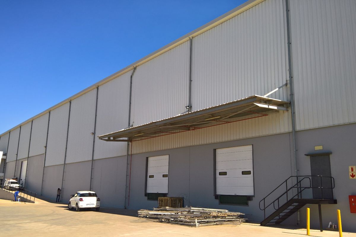 Industrial warehouse exterior featuring large roller shutter doors, a loading bay canopy, and a spacious concrete yard area.