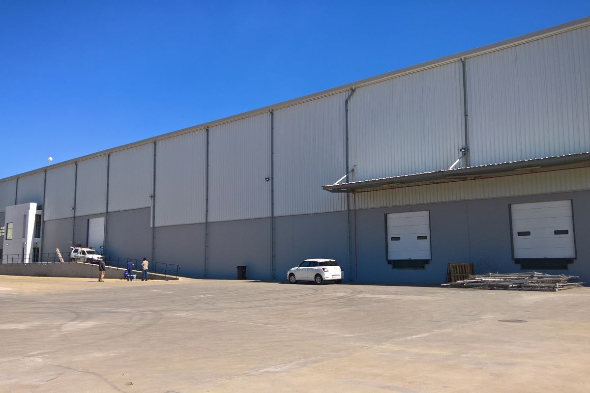 Industrial warehouse exterior featuring a large concrete yard, multiple roller shutter loading doors, and metal cladding facade.