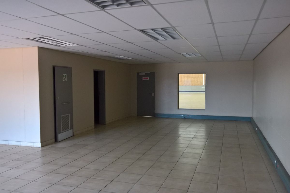 An open-plan industrial office space featuring a suspended ceiling, recessed lighting, and neutral ceramic floor tiles.