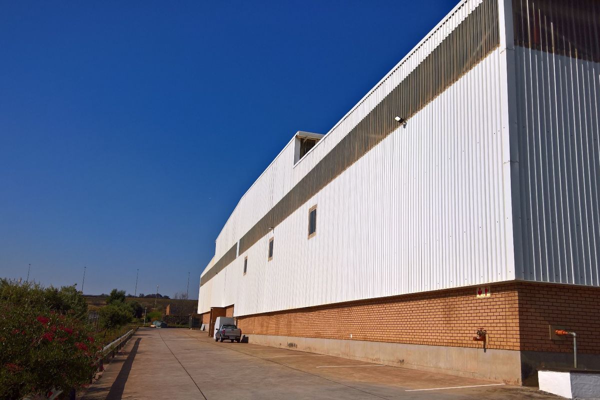 Side elevation of an industrial warehouse featuring corrugated metal cladding over a brick base with an adjacent concrete driveway.