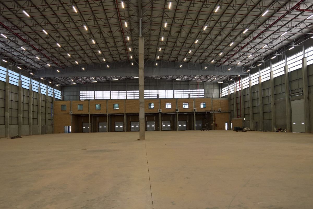 Spacious industrial warehouse featuring high ceilings, exposed steel trusses, concrete flooring, and multiple loading bay doors, suitable for logistics or manufacturing operations.