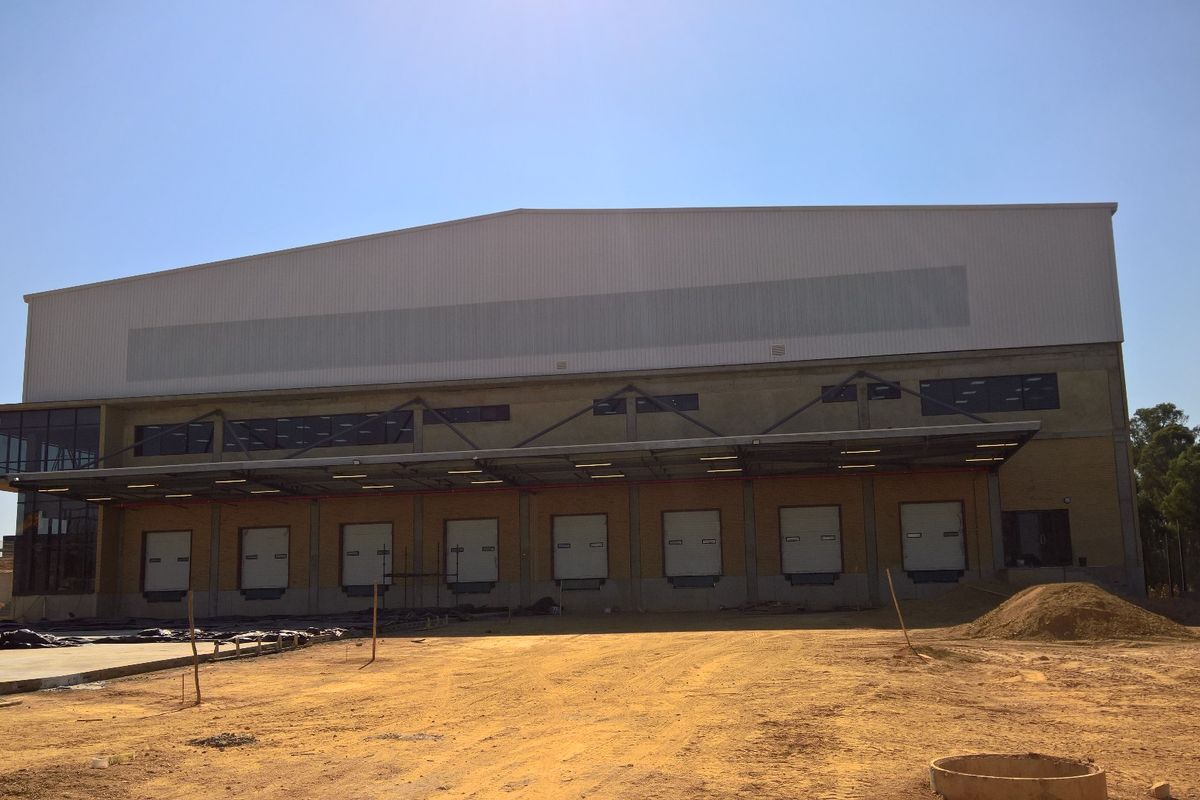 Industrial warehouse exterior featuring multiple loading docks with a protective steel canopy and metal cladding facade, set within an unfinished site.