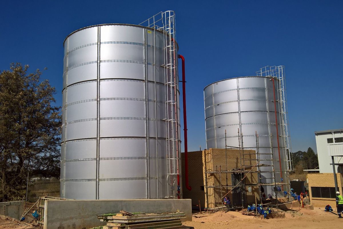 Industrial site featuring two large metal storage tanks with integrated access ladders and a brick pump house structure under construction.