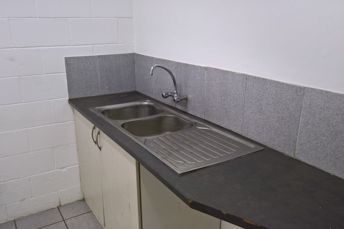 A functional kitchenette area featuring a stainless steel double sink, laminate countertop, tiled splashback, and built-in storage cabinetry.