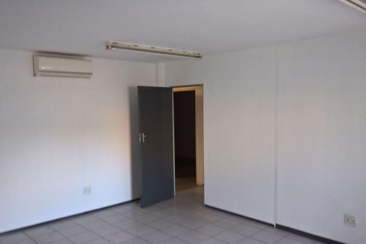 A clean, empty office space featuring tiled flooring, a wall-mounted air conditioning unit, and functional overhead lighting.