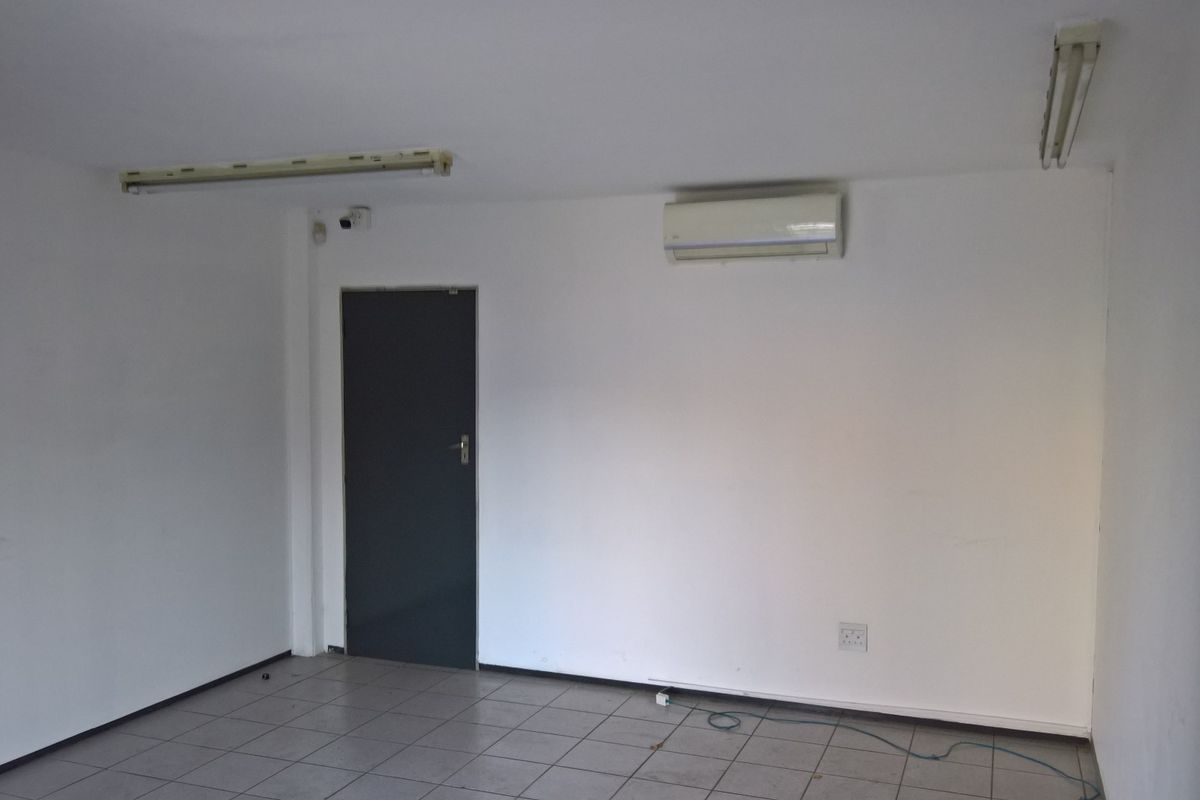 A functional, empty office space featuring tiled flooring, a wall-mounted air conditioning unit, and overhead fluorescent lighting.