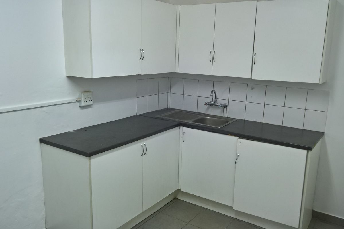 A functional kitchenette featuring white cabinetry, dark laminate countertops, a stainless steel double sink, and a tiled backsplash.