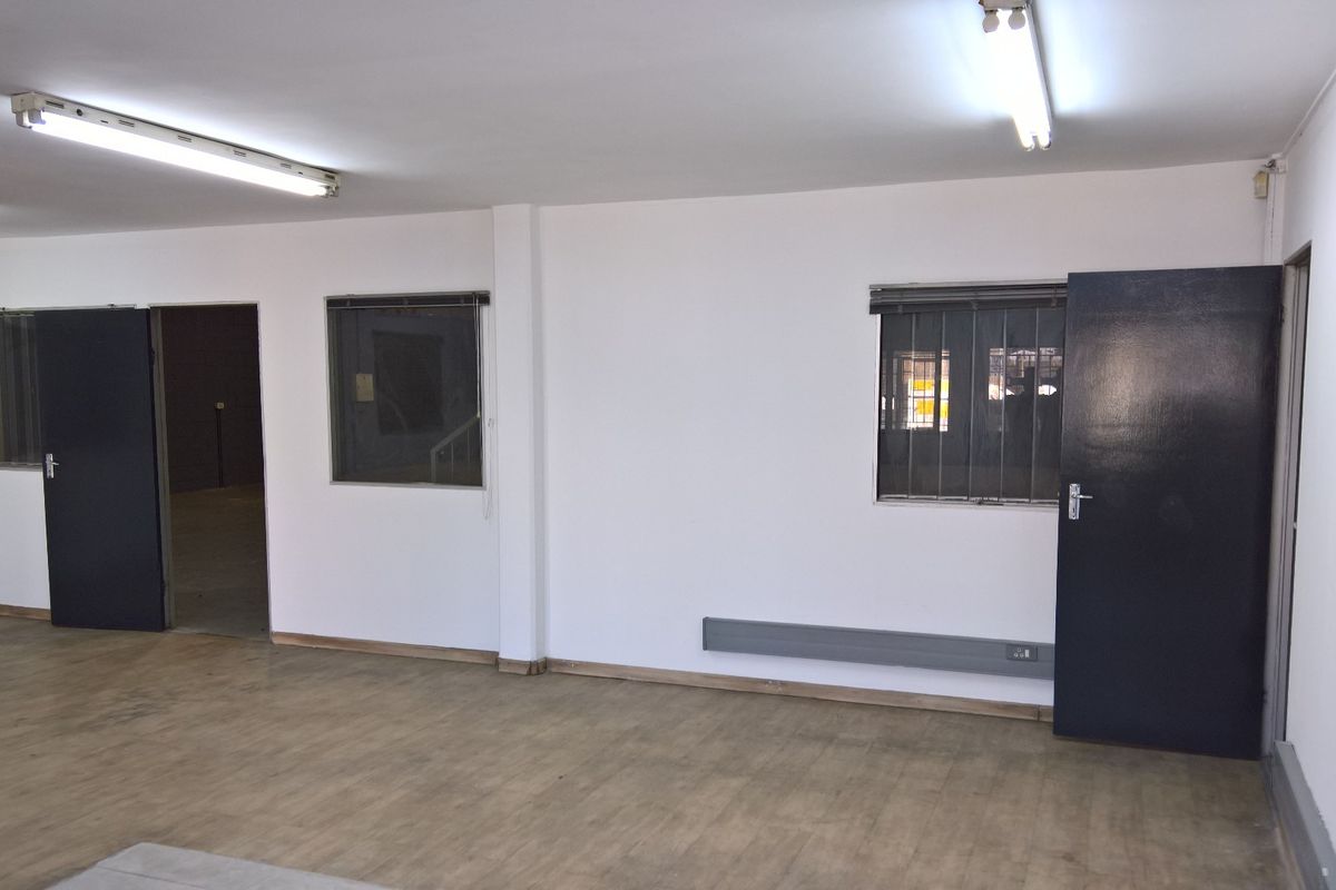 An empty, functional office space featuring laminate flooring, fluorescent lighting, and secure window bars, suitable for a variety of industrial or commercial uses.