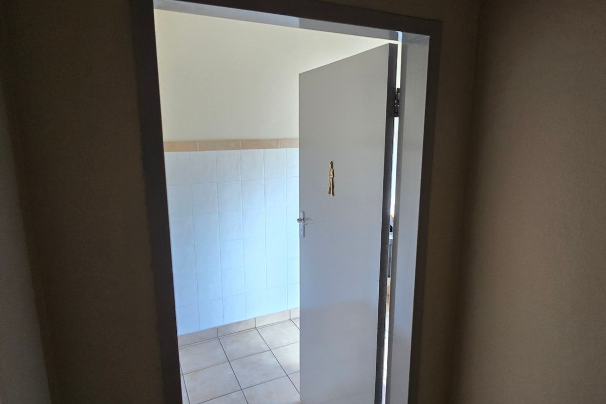 A view through a doorway into a functional bathroom space featuring tiled flooring and partial wall tiling.