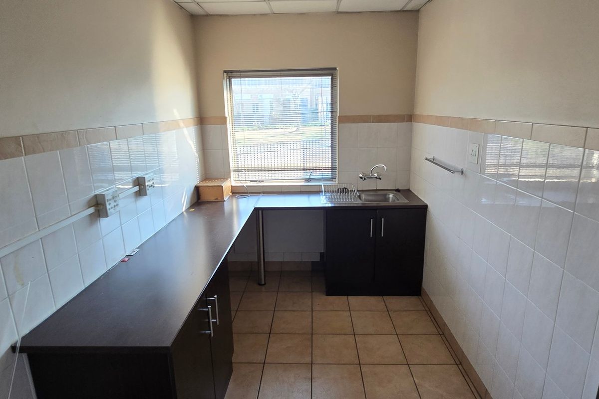 A functional kitchenette featuring dark cabinetry, laminate countertops, a stainless steel sink, and tiled finishes, suitable for office or industrial utility use.