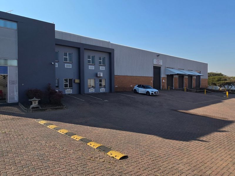 Front exterior view of an industrial property featuring a paved driveway, loading bays, and a modern office entrance section.