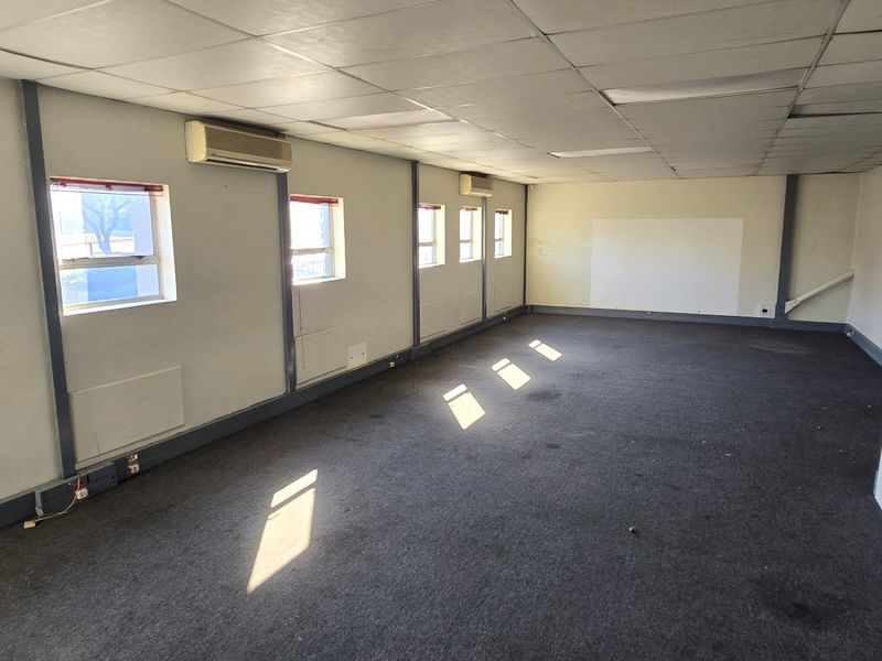 An empty industrial office space featuring suspended ceilings, split-system air conditioning units, and carpeted flooring, ready for refurbishment.