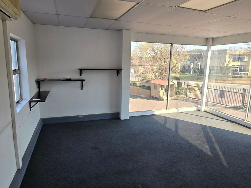 Bright, empty office space featuring large glass windows, suspended ceiling, wall-mounted air conditioning, and fitted shelving, suitable for a professional workspace.