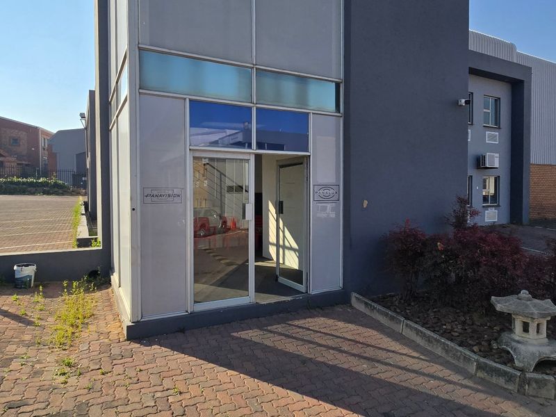 Front entrance of an industrial property featuring a glass door, paved access area, and external wall-mounted air conditioning unit.