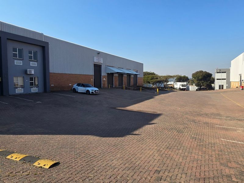 Spacious industrial yard featuring paved driveway, multiple loading bays with roller shutter doors, and external wall-mounted air conditioning units.