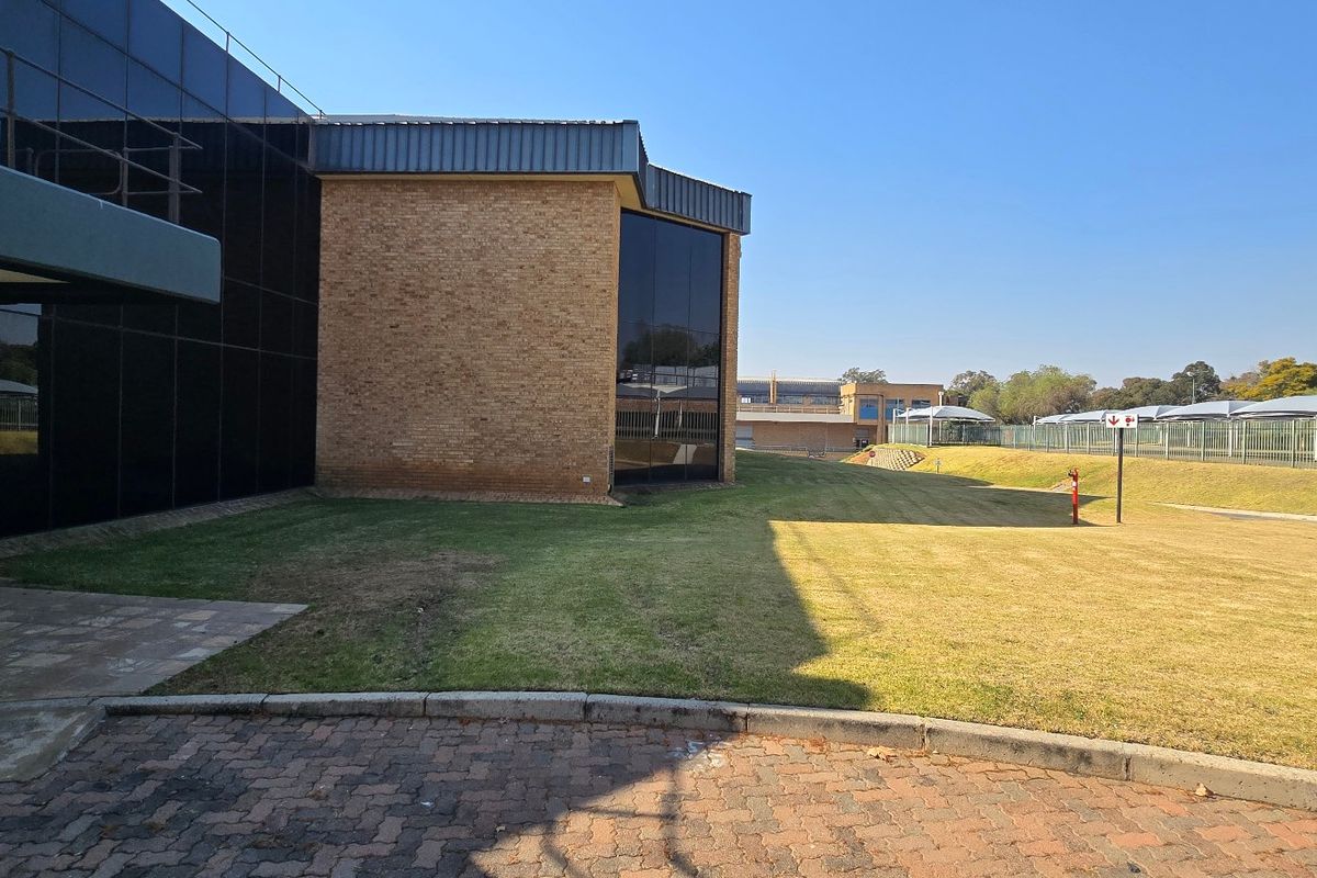 Exterior view of an industrial property featuring a combination of brick and glass curtain wall facade with surrounding paved areas and landscaped grounds.
