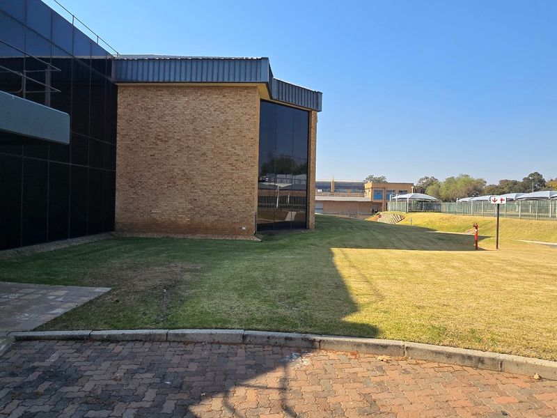 Exterior view of an industrial property featuring a combination of brick and glass curtain wall facade with surrounding paved areas and landscaped grounds.