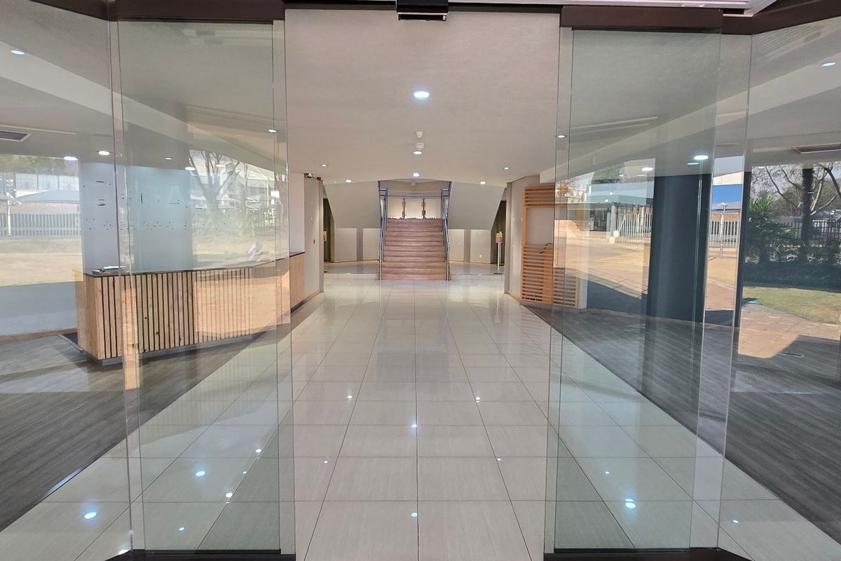 Spacious modern entrance lobby featuring glass sliding doors, polished tile flooring, a built-in reception desk, and a central staircase leading to the upper level.