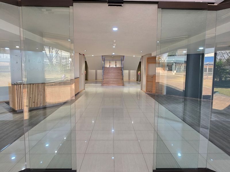 Spacious modern entrance lobby featuring glass sliding doors, polished tile flooring, a built-in reception desk, and a central staircase leading to the upper level.
