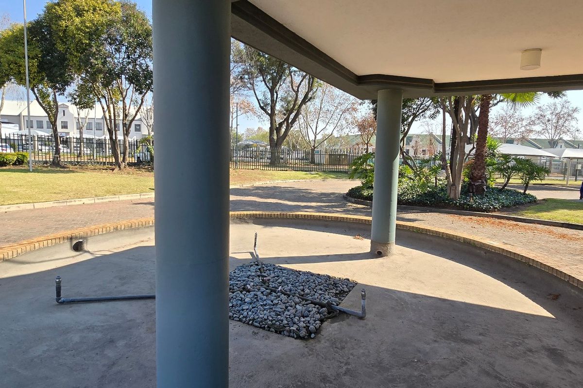 A covered outdoor patio area featuring concrete columns and a central unfinished feature space, overlooking the industrial property grounds and security fencing.