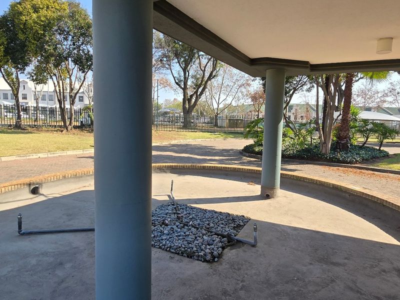A covered outdoor patio area featuring concrete columns and a central unfinished feature space, overlooking the industrial property grounds and security fencing.