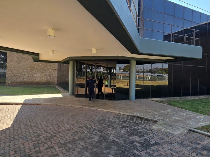 Front entrance of an industrial building featuring a covered canopy, brick facade, and modern glass curtain walling with a paved driveway.