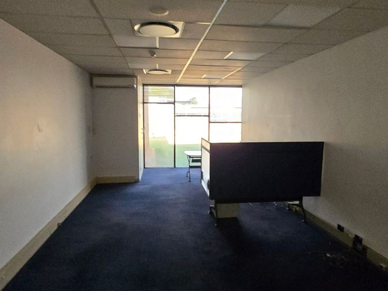 An empty office space featuring a suspended ceiling, recessed lighting, split-system air conditioning, and large windows providing natural light.