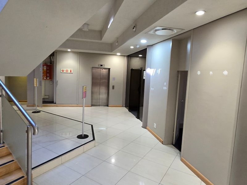 Modern industrial building lobby featuring a staircase with glass balustrades, tiled flooring, and elevator access.