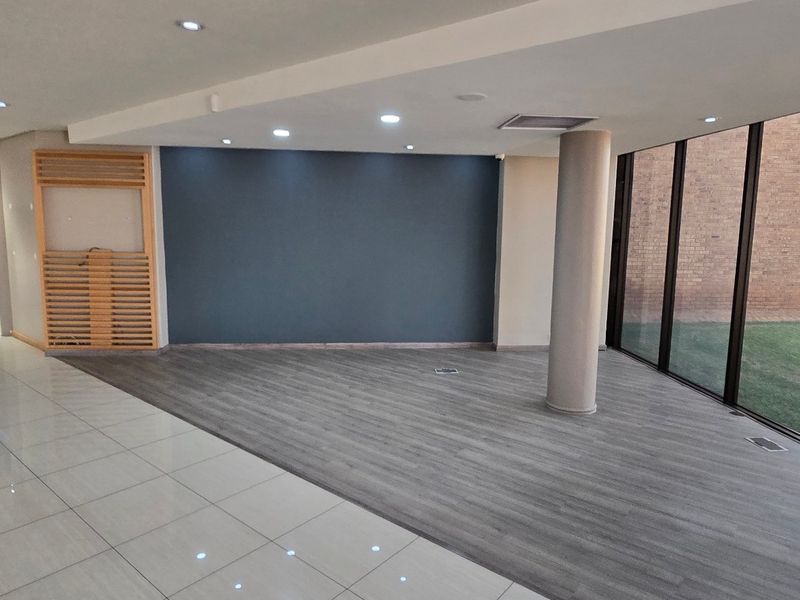 Spacious open-plan industrial office area featuring floor-to-ceiling windows, a mix of tiled and laminate flooring, and modern recessed lighting.