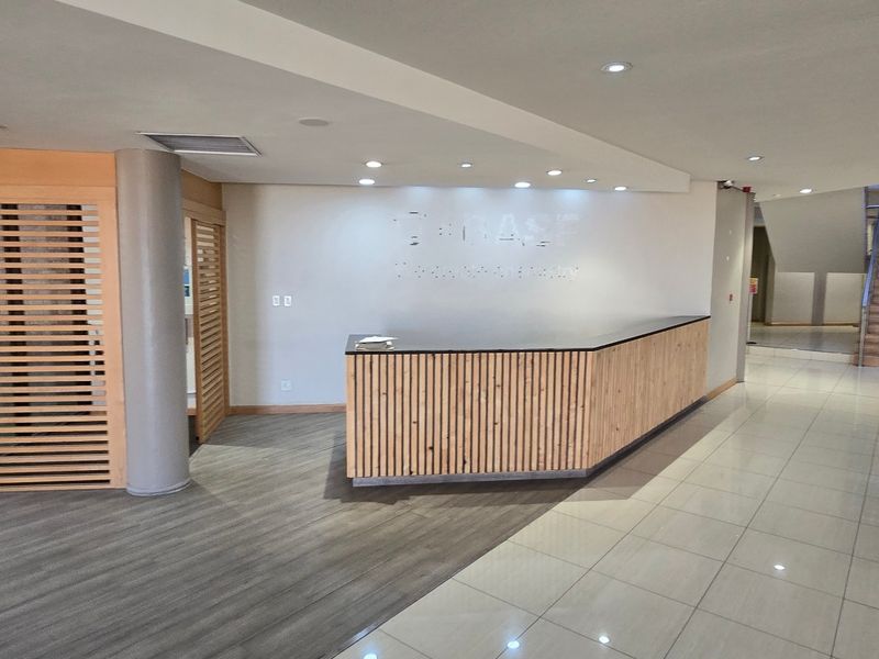 Modern industrial reception area featuring a custom timber-slatted desk, tiled and laminate flooring, and an open staircase leading to the upper level.