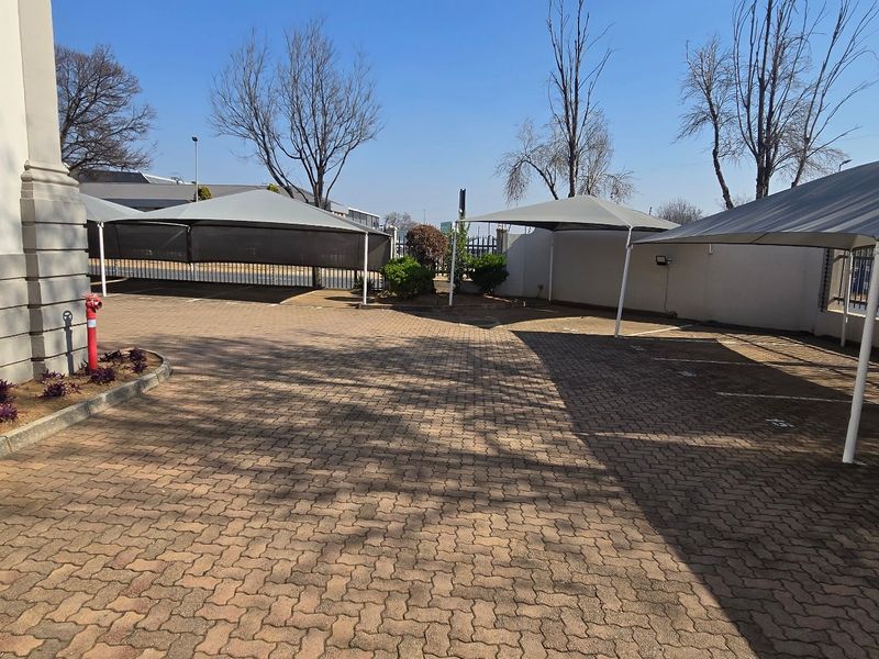 A well-maintained industrial parking area featuring paved surfaces, multiple shade cloth carports, and perimeter security fencing.