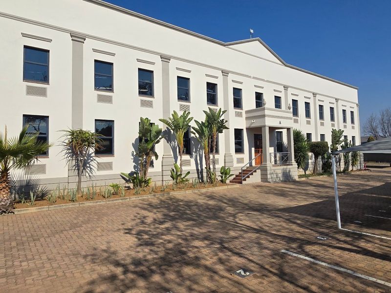 A well-maintained multi-story industrial office building featuring a paved driveway, covered parking bays, and professional landscaping at the front entrance.
