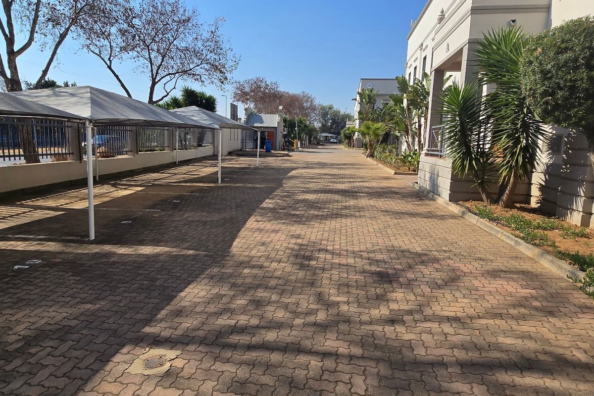 A well-maintained industrial property exterior featuring a paved driveway with covered parking bays and established landscaping along the building facade.