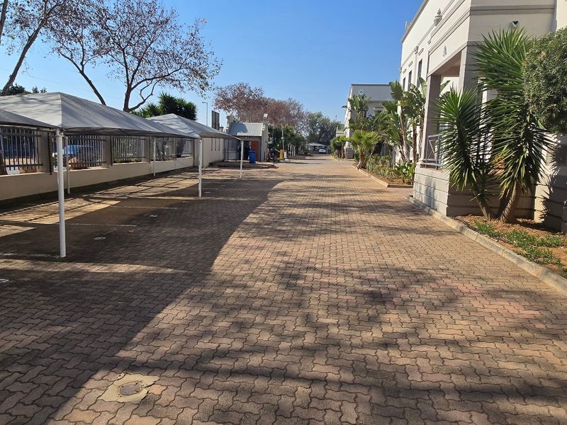 A well-maintained industrial property exterior featuring a paved driveway with covered parking bays and established landscaping along the building facade.