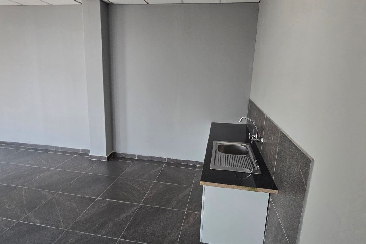 A clean, minimalist kitchenette area featuring dark tiled flooring, a modern sink with faucet, and a tiled splashback in an industrial space.