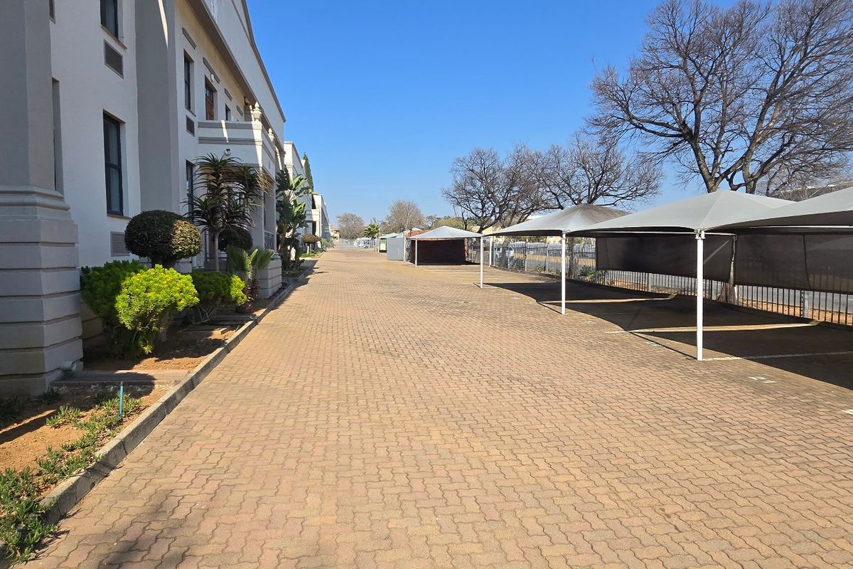 Exterior view of an industrial property featuring a paved driveway, designated parking bays with shade cloth structures, and perimeter fencing.