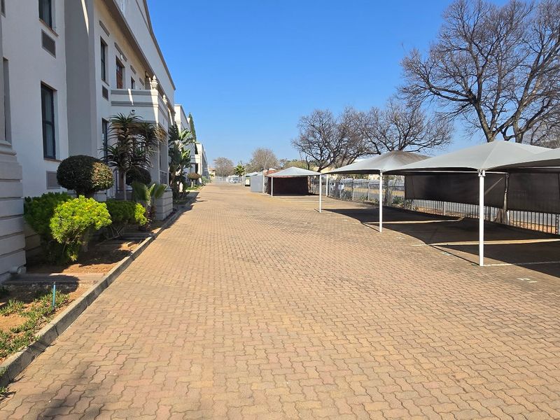 Exterior view of an industrial property featuring a paved driveway, designated parking bays with shade cloth structures, and perimeter fencing.