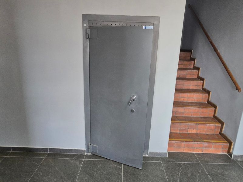 A clean industrial hallway featuring a heavy-duty steel security door and a brick staircase with a wooden handrail.