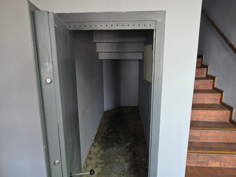 A secure utility storage area featuring a heavy-duty steel vault door, adjacent to a staircase with brick treads and a wooden handrail.