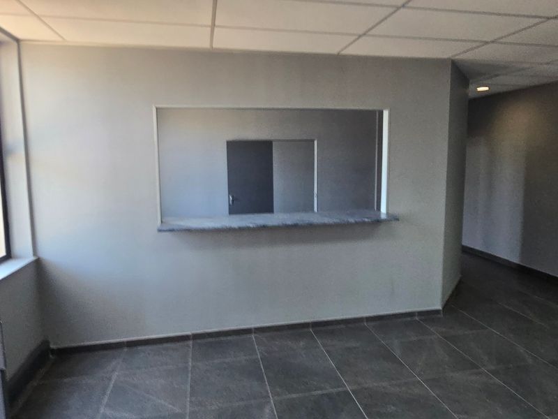 An empty office space featuring tiled flooring, a built-in service counter, and a suspended ceiling, suitable for administrative or industrial reception use.