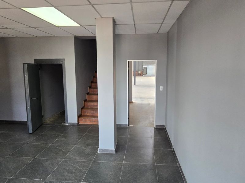 An open-plan industrial office space featuring modern grey tiled flooring, a suspended ceiling with recessed lighting, and access to a secure storage area.