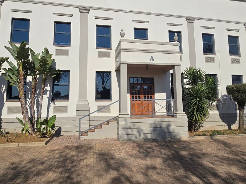 Front elevation of a professional industrial building featuring a covered entrance portico, paved driveway, and symmetrical architectural detailing.