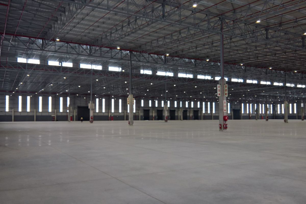 Expansive industrial warehouse space featuring high ceilings with exposed steel trusses, polished concrete floors, and integrated fire safety systems.