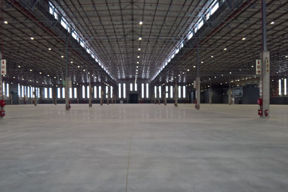 A large, open-plan industrial warehouse space featuring polished concrete floors, exposed steel roof trusses, and high-bay lighting.