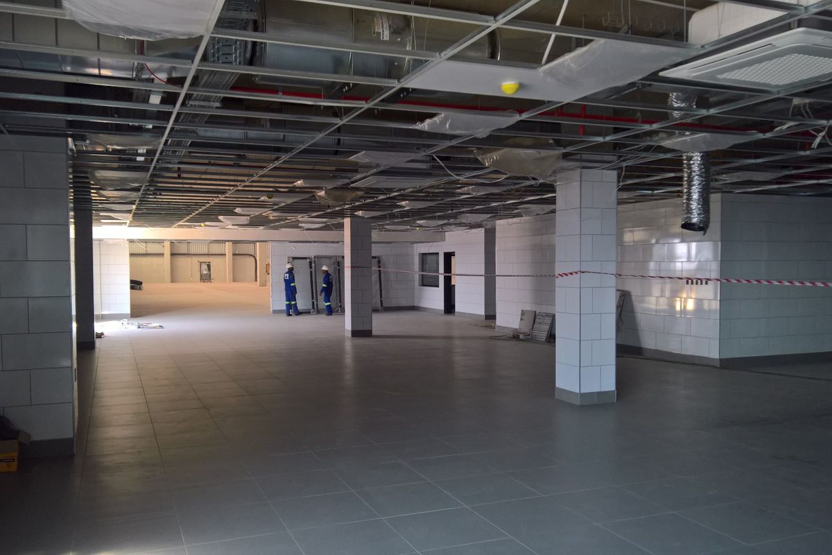 Large open-plan industrial space currently under construction, featuring tiled flooring, tiled support columns, and an exposed ceiling grid with visible HVAC and fire systems.