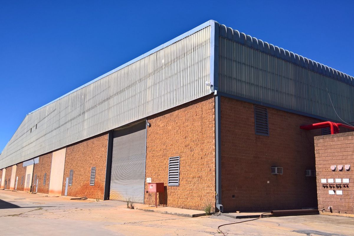 Exterior view of an industrial warehouse featuring brick and corrugated metal construction, roller shutter access, and external fire safety infrastructure.