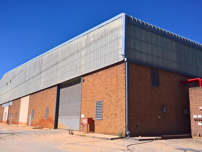 Exterior view of an industrial warehouse featuring brick and corrugated metal construction, roller shutter access, and external fire safety infrastructure.