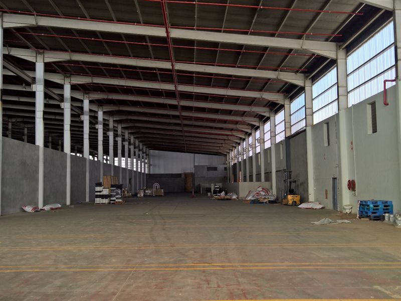 Spacious industrial warehouse featuring a high-clearance steel portal frame, concrete flooring, fire sprinkler system, and natural light through translucent roof panels.