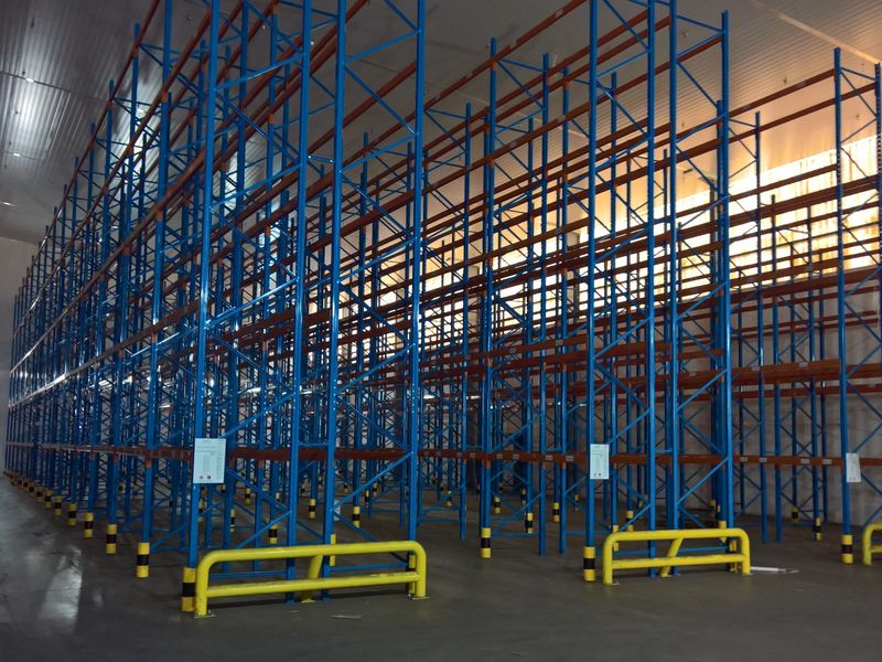 Spacious industrial warehouse interior featuring extensive high-density pallet racking systems, concrete flooring, and protective steel safety bollards.